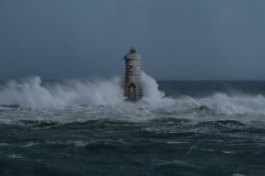 Powerful waves crashing against a Mangiabarche lighthouse during a hurricane, symbolizing resilience and the forces of nature