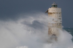 Powerful waves crashing against a Mangiabarche lighthouse during a hurricane, symbolizing resilience and the forces of nature