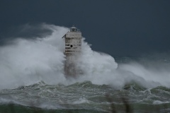 Powerful waves crashing against a Mangiabarche lighthouse during a hurricane, symbolizing resilience and the forces of nature